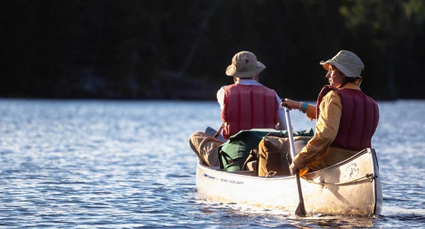 Two people wearing lifejackets paddle a canoe